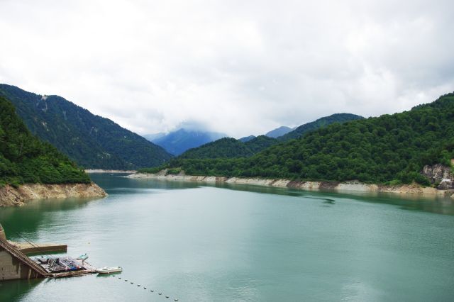 ダムの堤防から黒部湖を眺める。自然風景が広がる。