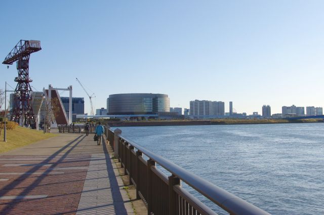 南側へ川沿いを戻っていく。奥に見えるのは新豊洲駅変電所・テプコ豊洲ビル（ビッグドラム）。