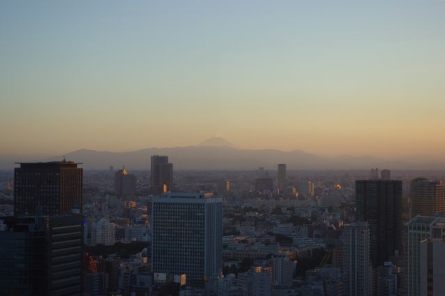 日が沈む西側の夕景。ビル群は一面夕陽色に照らされ、奥の山並みからは富士山が顔をだしている。