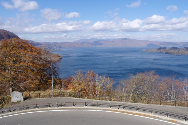 紅葉した山々に囲まれた十和田湖の開放的な眺め。風が強く波が立っています。