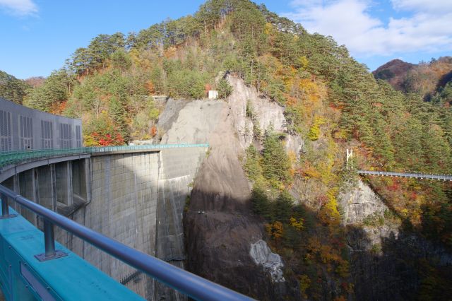ダムの峡谷側へ。山は岩肌に紅葉があり、谷には吊り橋があります。