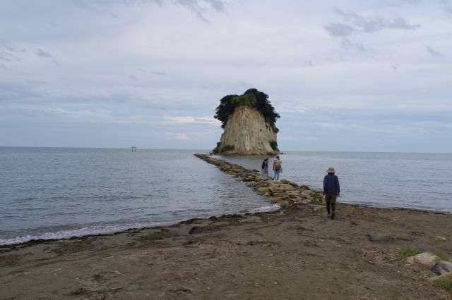 波の音がする穏やかな海岸、伸びる石の道の先にある見附島。