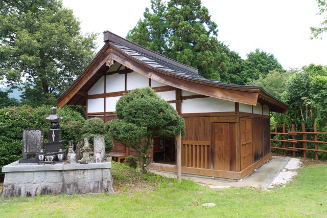 厩の建物、独特な屋根形状。手前には田峯城戦没、病没諸霊供養塔。