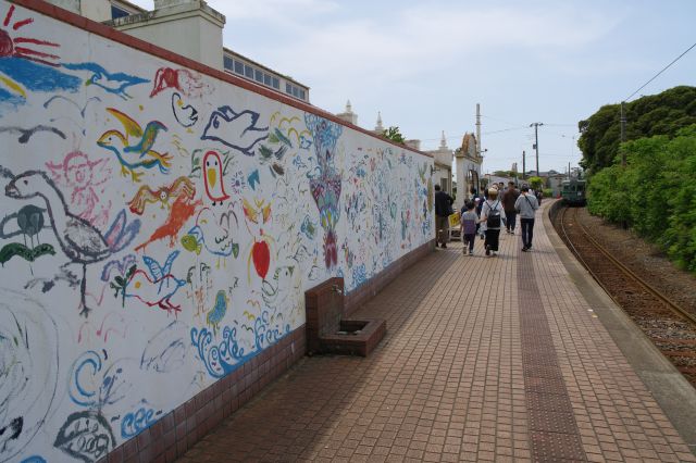 壁に描かれたカラフルな絵があります。乗客は駅舎へと流れていきます。